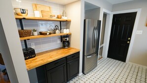Eine Küche mit Holzausziehtisch, schwarzen Schränken, einem Edelstahlkühlschrank und einem gefliesten Boden.