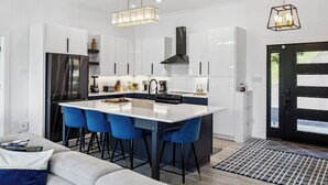 Een moderne keuken met witte kastjes, een zwarte koelkast en blauwe barstoelen.