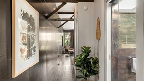 A hallway with a large framed abstract painting, a potted plant, and a door leading to a room with a view of greenery. - Urban Escape Glebe House (Glebe)