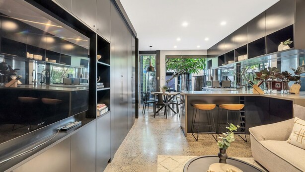 A modern kitchen with a central island, bar stools, and a dining area with chairs. - Urban Escape Glebe House (Glebe)