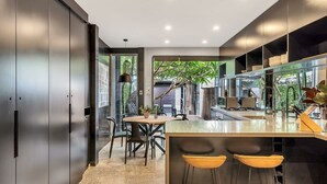 A modern kitchen with a central island, bar stools, and a dining area with chairs. - Urban Escape Glebe House (Glebe)