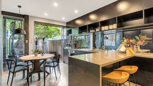A modern kitchen with a central island, black cabinets, and a dining area with a round table and chairs. - Urban Escape Glebe House (Glebe)