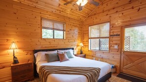 A wooden cabin bedroom with a bed, two bedside tables, and a ceiling fan. - Cozy cabin for 2, private hot tub, King size bed! (Overgaard)