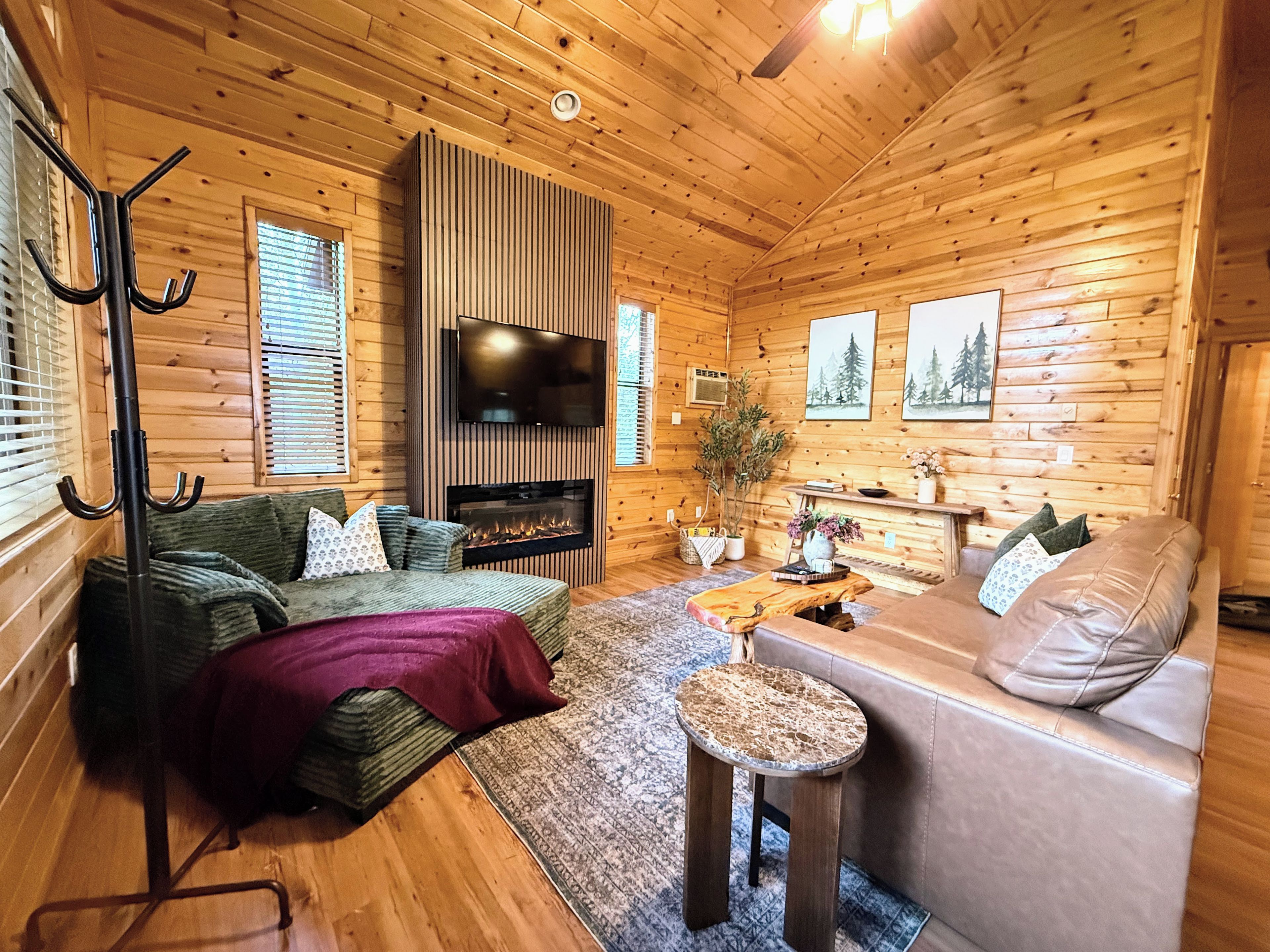 A cozy log cabin interior with a fireplace, a television, and a sofa.