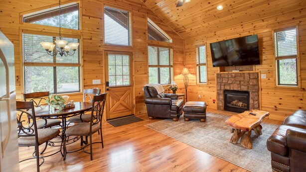 A wooden cabin interior with a dining area, seating, a fireplace, and a television. - Cozy cabin for 2, private hot tub, King size bed! (Overgaard)