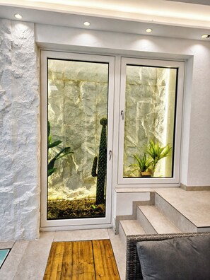 Una habitación con una puerta de cristal que da a un terrario de cactus, un pequeño banco de madera y una escalera.