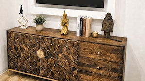 Un salon moderne avec un meuble en bois, un téléviseur à écran plat fixé au mur et des objets décoratifs posés sur le meuble.