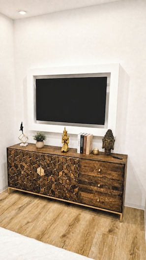 Een moderne woonkamer met een houten kast, een flatscreen televisie aan de muur en decoratieve objecten op de kast.