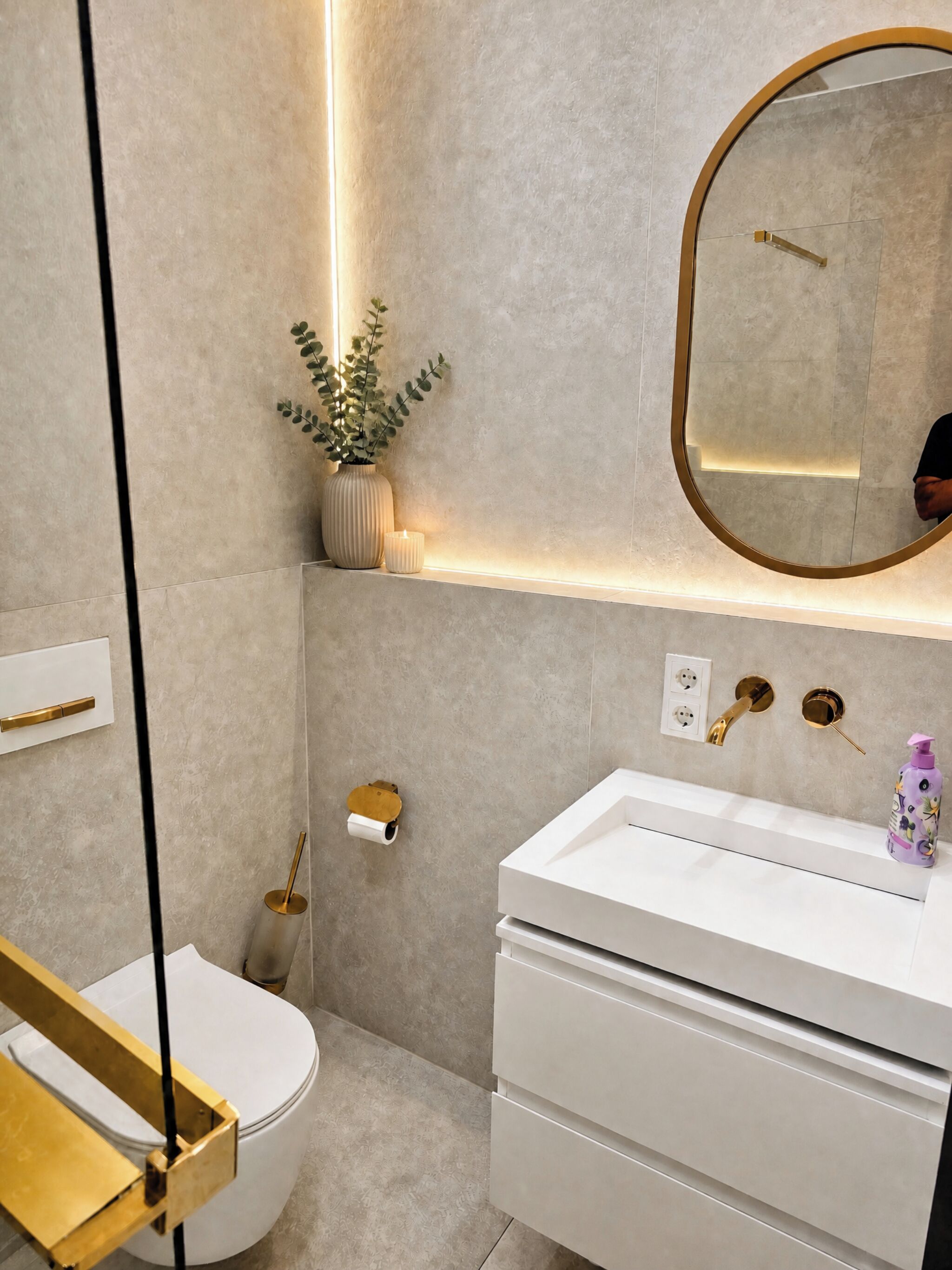 Une salle de bain moderne avec un lavabo blanc, un miroir à cadre doré, des toilettes et un distributeur de serviettes fixé au mur.