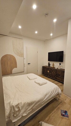 A modern bedroom with a large bed, a dresser, a flat-screen TV, and a ceiling light. - UG Neubau City Wohnung (optional Pool+Gym+2tes Bad extra buchbar) (Munich)
