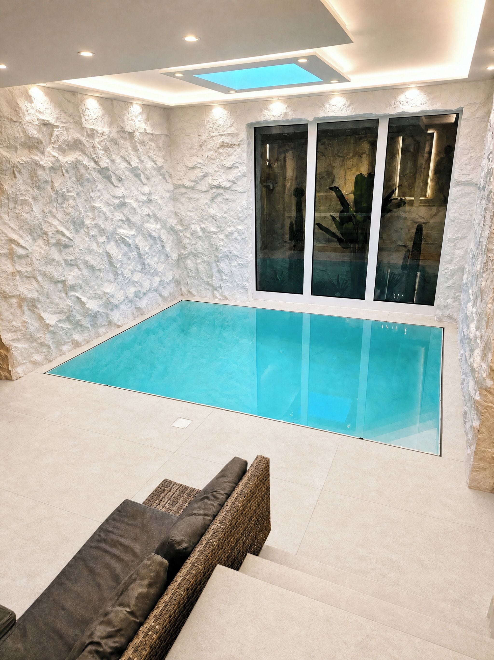 En swimmingpool med et glasomkranset område, omgivet af en struktureret væg og et loft med indbygningsbelysning.