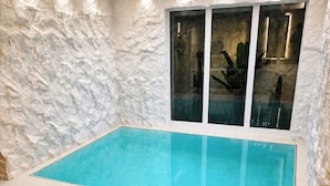 Une piscine dotée d’une enceinte en verre, entourée d’un mur à texture et surmontée d’un plafond avec des luminaires encastrés.