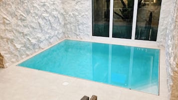 En swimmingpool med et glasomkranset område, omgivet af en struktureret væg og et loft med indbygningsbelysning.