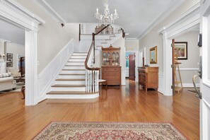 Una majestuosa escalera con candelabro, armarios de madera y un rug con diseño en un pasillo amplio.