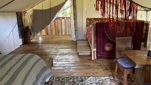 Un hébergement sous tente doté d’un plancher en bois, d’un lit avec une couverture à rayures, d’une table à manger avec des chaises et d’un élément décoratif suspendu.
