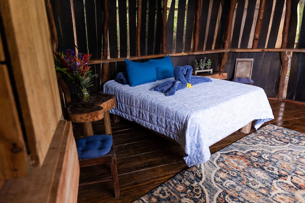 Une pièce rustique en bois, avec un lit, une petite table sur laquelle est posé un vase de fleurs et une chaise.
