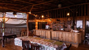 Un intérieur rustique en bois, avec un coin bar, des tables et des chaises en bois, et une structure en forme de tente en arrière-plan.
