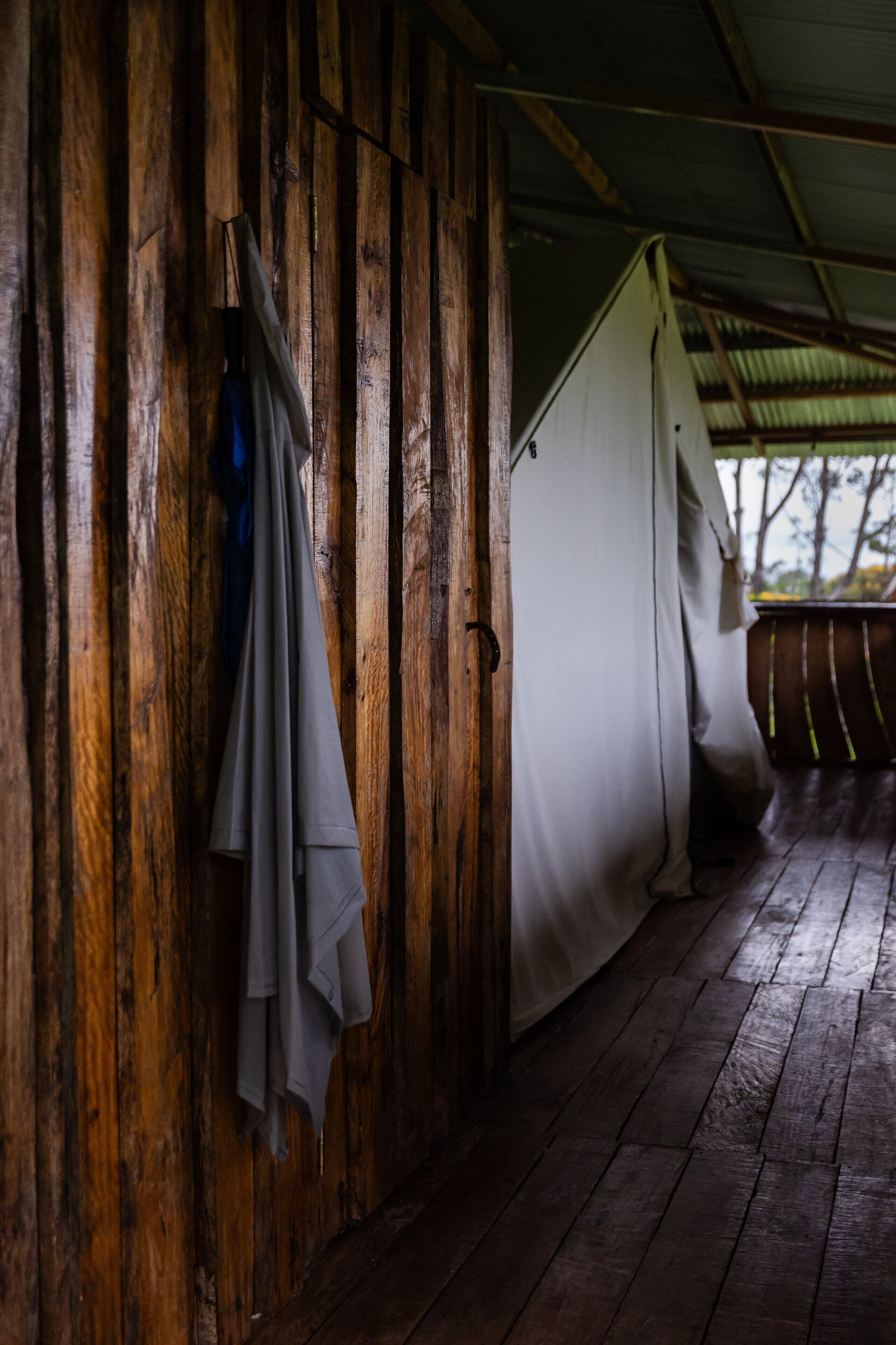 A wooden cabin with a covered porch, a white tent-like structure, and a hanging cloth.