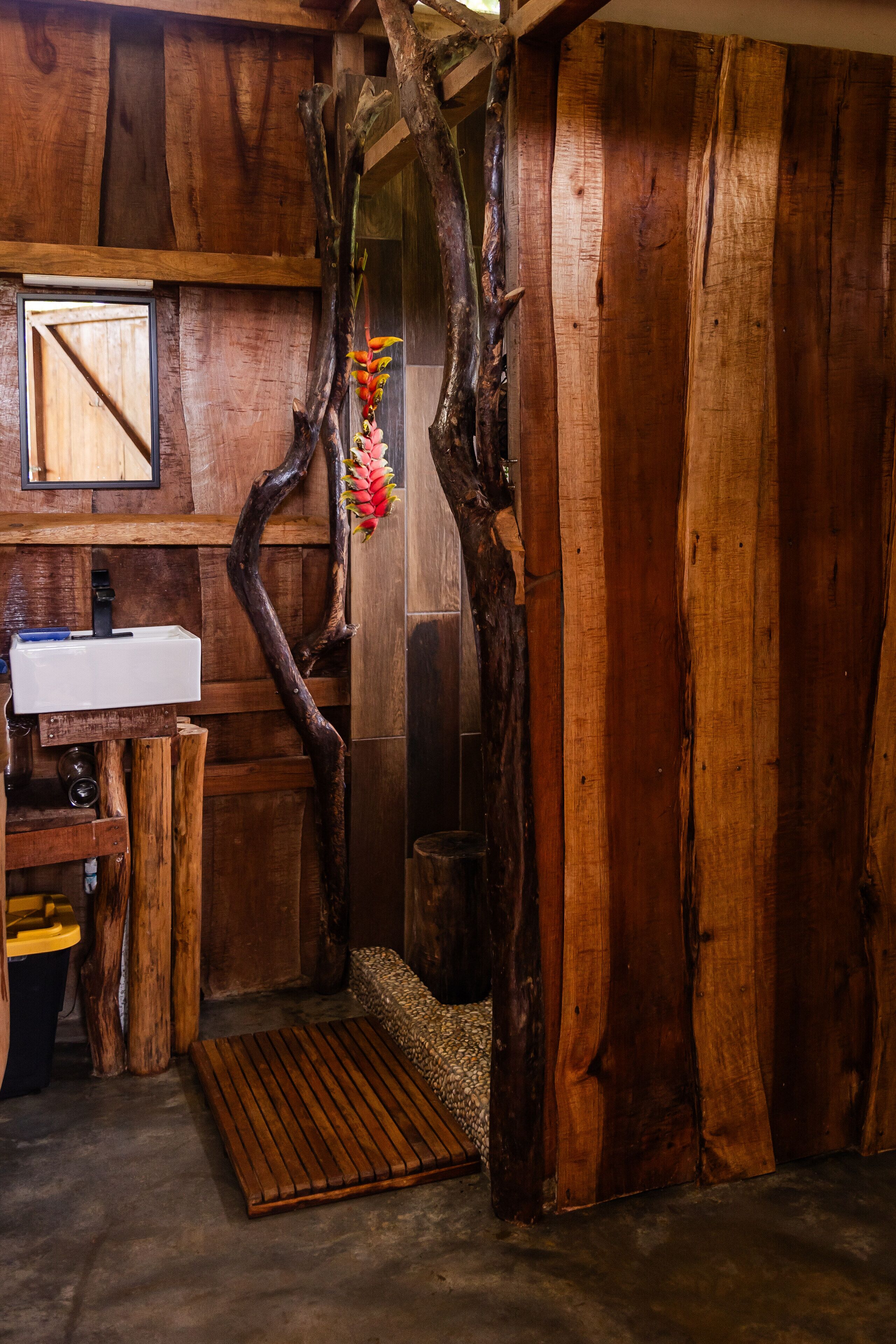 A rustic bathroom with a wooden tree trunk wall, a sink, and a mirror.