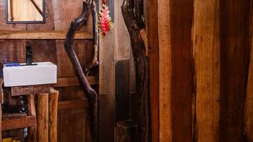 A rustic bathroom with a wooden tree trunk wall, a sink, and a mirror.