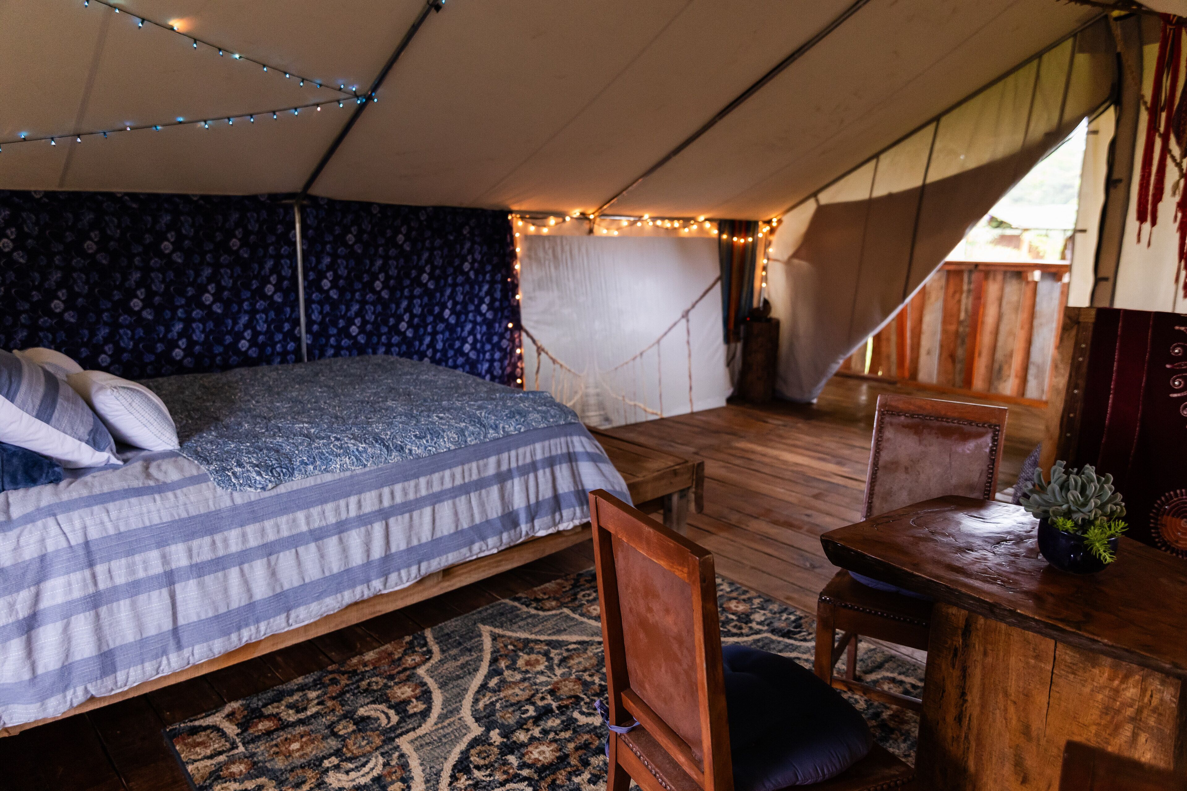 A tented accommodation with a bed, a table, and chairs.