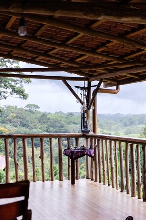 Una terraza de madera con una estatua de Buda y una mesa, con vistas a un paisaje boscoso.