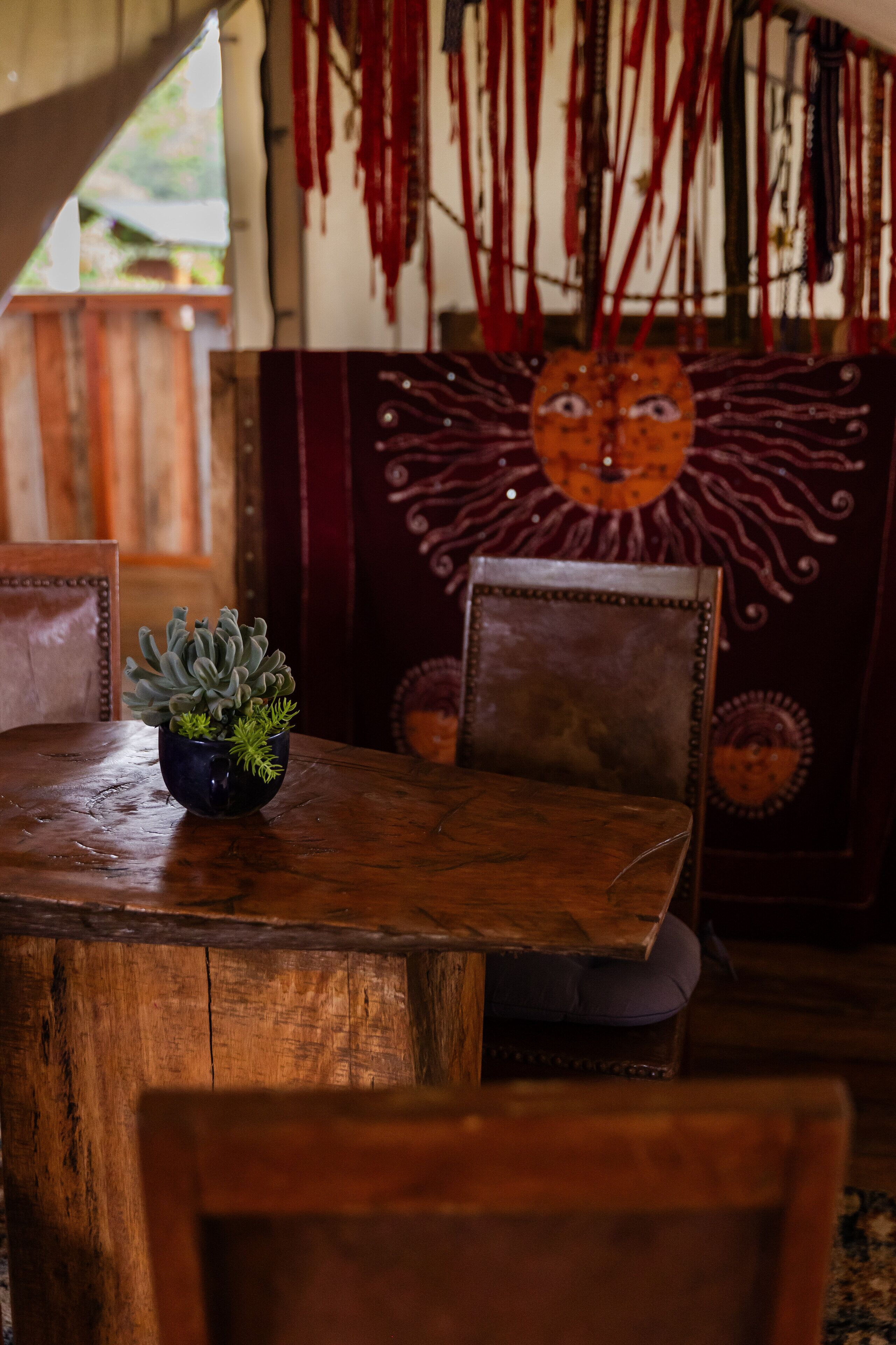 A wooden table with a potted plant, a chair, and a wall with a decorative mask.