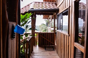 Un pasillo de madera con vistas al exterior, un cubo azul y una puerta con cerradura.
