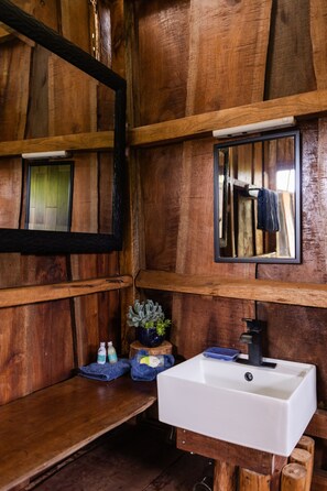 Un baño rústico de madera con un lavabo blanco, un espejo y un perchero para toallas.