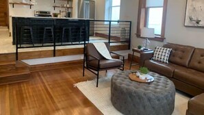 A modern living room with a brown leather sofa, a grey ottoman, and a wooden floor. - Luxury Living in Downtown Le Mars (Le Mars)
