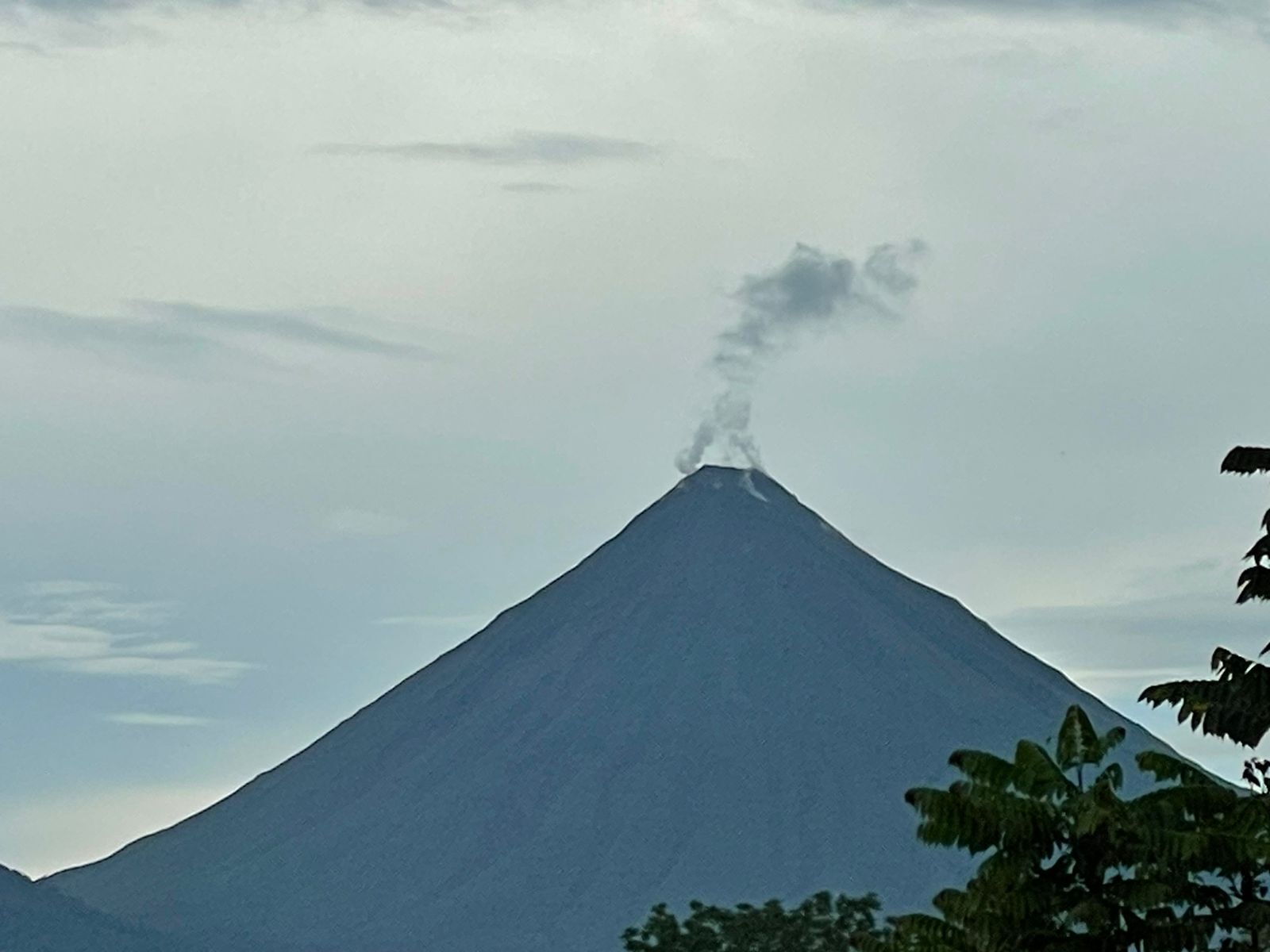 Una montaña con una columna de humo visible, rodeada por un cielo nublado.