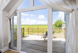 Een kamer met een grote schuifglazen deur die uitkomt op een terras met een houten schutting en een grasveld.