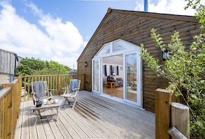Een houten terras met buitenmeubilair, een schuifdeur naar een kamer en uitzicht op groen.
