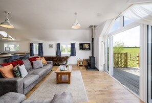 A spacious living room with a grey sofa, wooden coffee table, and a large window offering a view of the outdoors.