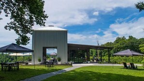 Un'area pranzo all'aperto moderna con una zona salotto coperta, un edificio centrale con una porta in vetro e un vialetto che conduce all'ingresso.