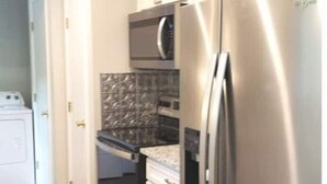 Una cucina compatta con frigorifero in acciaio inox, forno a microonde e forno integrato.