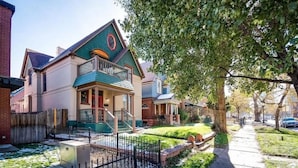 A two-story house with a green roof, a front porch, and a fenced yard.