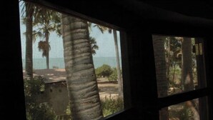 A window view of a tropical landscape with palm trees and a building in the distance. - Nemasu ecolodge: breathtaking!l (Gunjur)