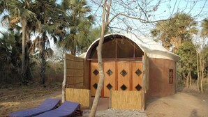 A small, rustic hut with a thatched roof, wooden door, and two benches outside. - Nemasu ecolodge: breathtaking!l (Gunjur)