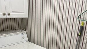 Un área de lavandería compacta con lavadora de carga frontal, un tendedero y un aspirador.