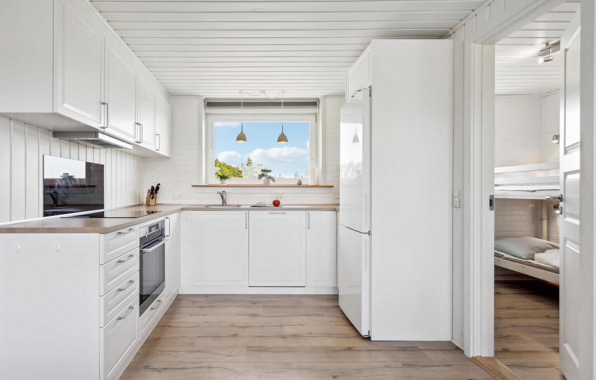 Eine moderne Küche mit weißen Schränken, einem Einbauofen und einem Fenster mit Blick auf Grünflächen.