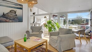 Ein geräumiges Wohnzimmer mit einem Holztisch, grauen Sofas und einem großen Fenster mit Blick ins Freie.