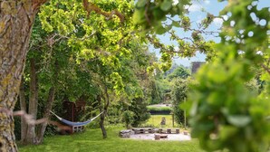 Ein Garten mit einer Hängematte, Picknicktischen und einem kleinen Gebäude.