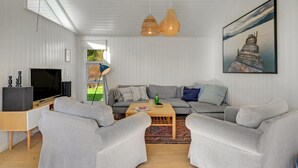Ein modernes Wohnzimmer mit einer grauen Sofagarnitur, einem Couchtisch, einem Fernseher und einem Gemälde mit einer K üstenlandschaft.