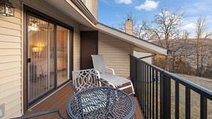 A balcony with a table and two chairs, a sliding glass door, and a view of trees and hills. - Pointe Royale, Step Free Entry, Indoor Pool (Branson)
