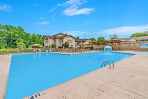 A swimming pool with a 4 FT depth marker, a covered seating area, and a building with a stone facade. - Walk-In Pointe Royale | Indoor Pool + Fireplace (Branson)