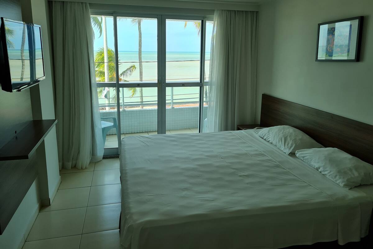 Une chambre d’hôtel avec un lit, une télévision, une vue sur la plage et un balcon.