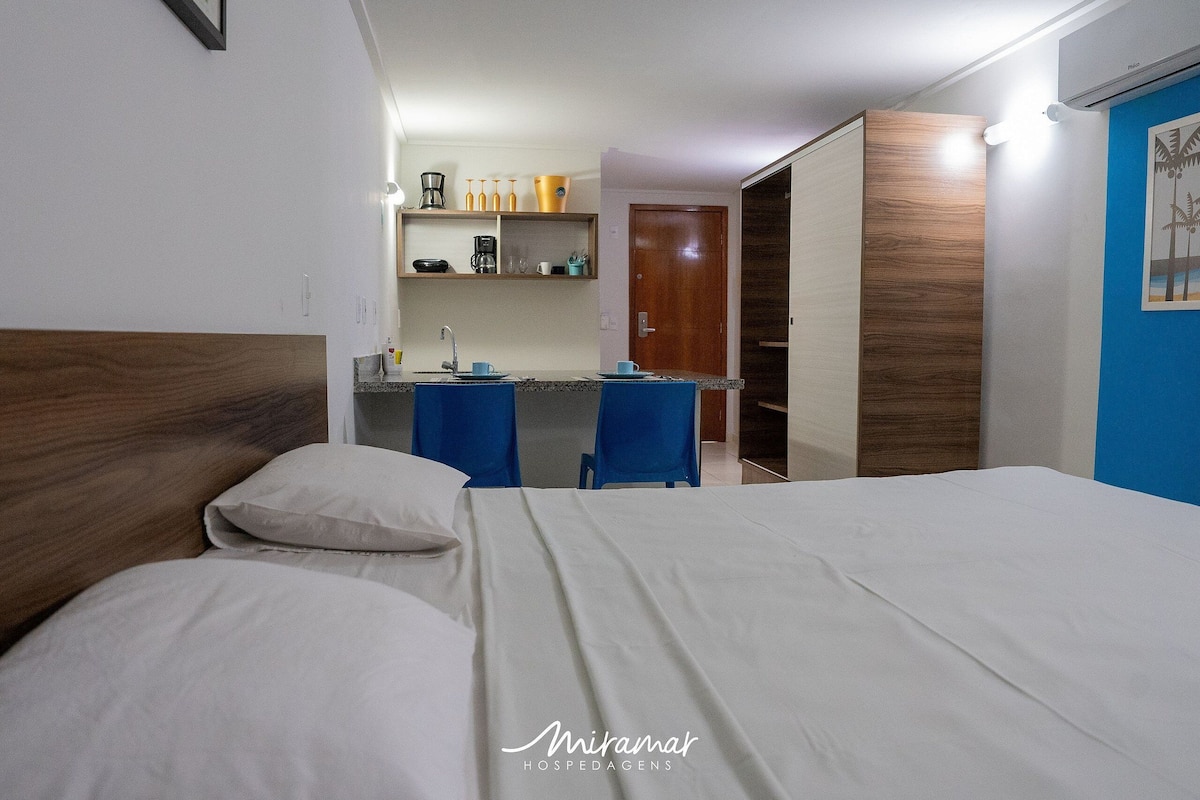 Une chambre d’hôtel comprenant un lit, un bureau avec une chaise, une kitchenette et une armoire.