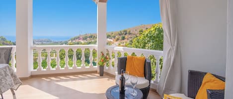 Un balcon avec une balustrade blanche, des meubles en osier et une table sur laquelle se trouvent une bouteille et des verres.