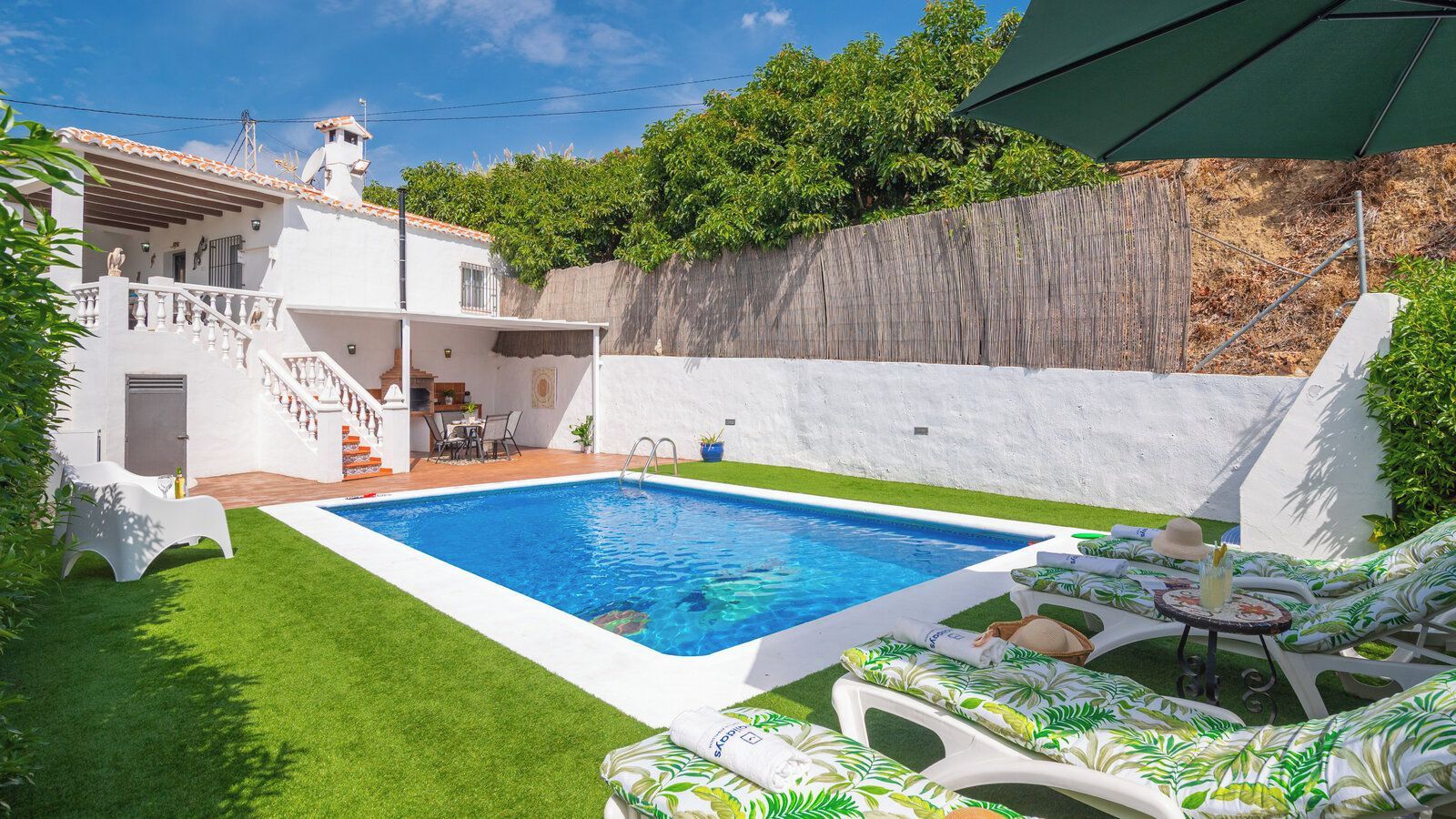 Une piscine dotée d’une terrasse blanche, entourée d’une pelouse bien entretenue et d’une clôture en bois.